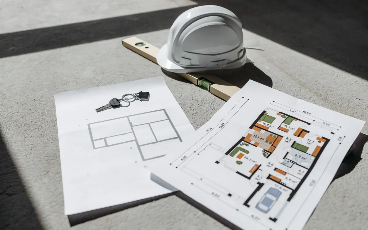 Building plans, a hard hat, and keys on a table
