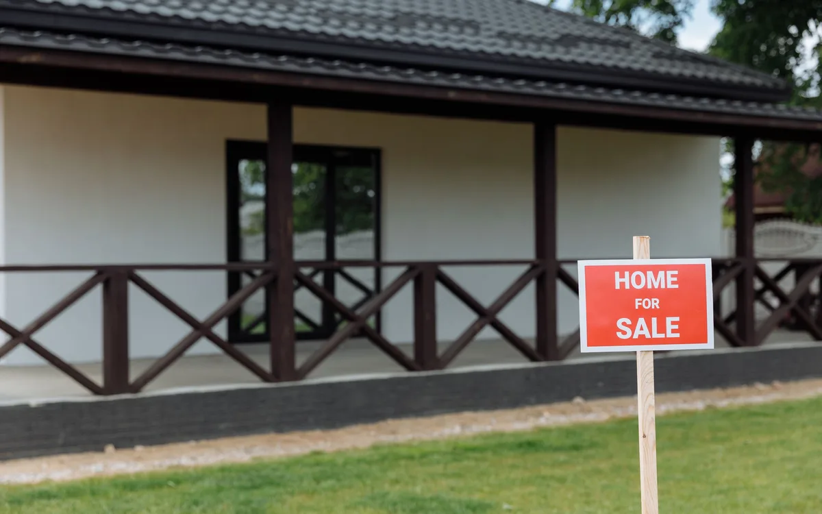 White house with a dark roof and a Home for Sale sign in the front yard